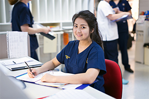 A female nurse sits at a desk reviewing medical records.