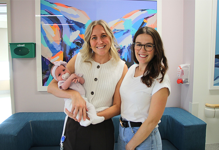 Midwife Ebony holding baby Holly, alongside mother Tara, smiling. 