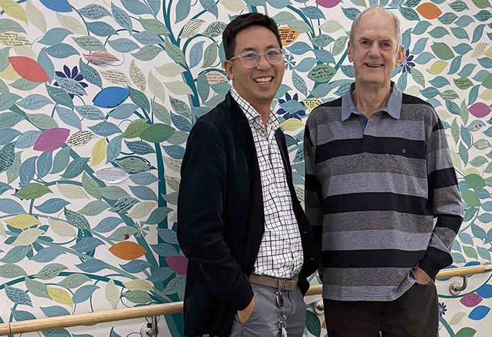 Dr Wei-Sen Lam stand with a patient, Barry, in front of a colourful wall mural