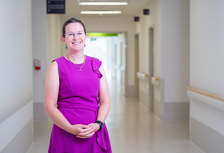 Merrilee standing in the corridor of a ward, wearing a lilac dress.