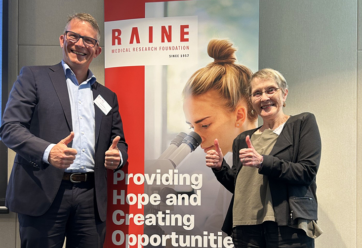 Dr Piers Truter (left) standing in front of a Raine Medical Research Foundation pull up banner. 