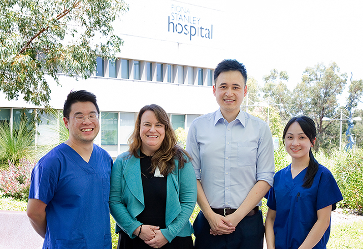 A team of four researchers stand together with a Fiona Stanley Hospital building in the background
